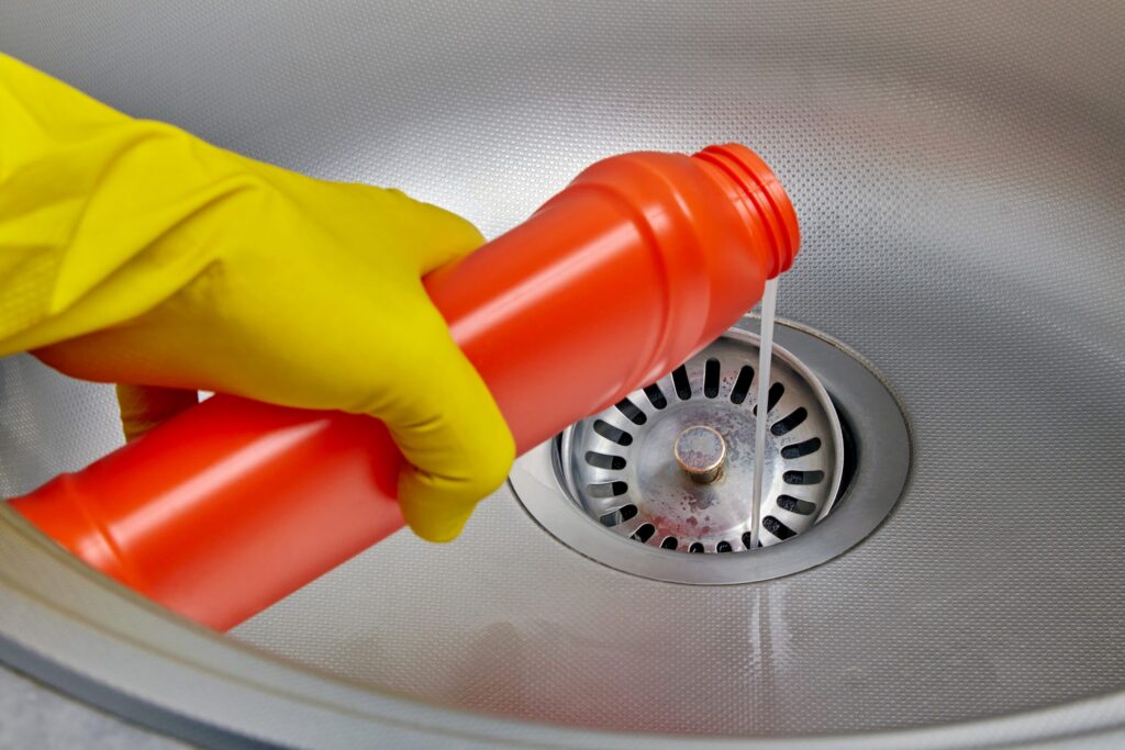 homeowner pouring chemical drain cleaner down kitchen sink