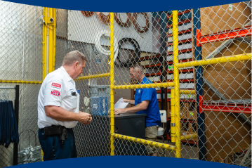 Financing paperwork is held by an HVAC technician at a desk with another technician walking next to the yellow chain fence separating the space